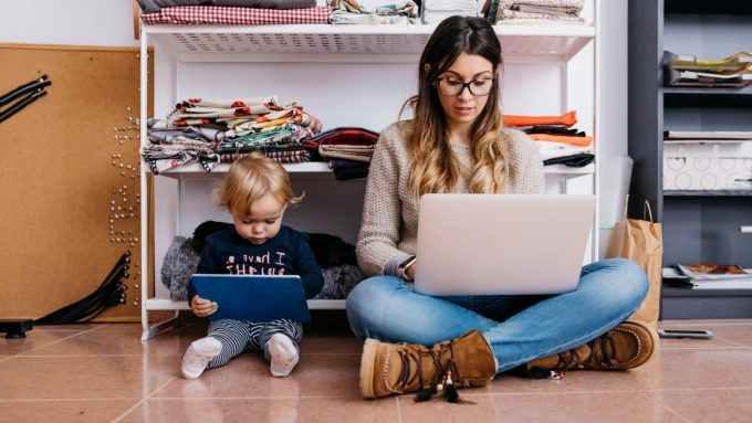 Mother and little daughter sitting on the floor at home using laptop and tablet